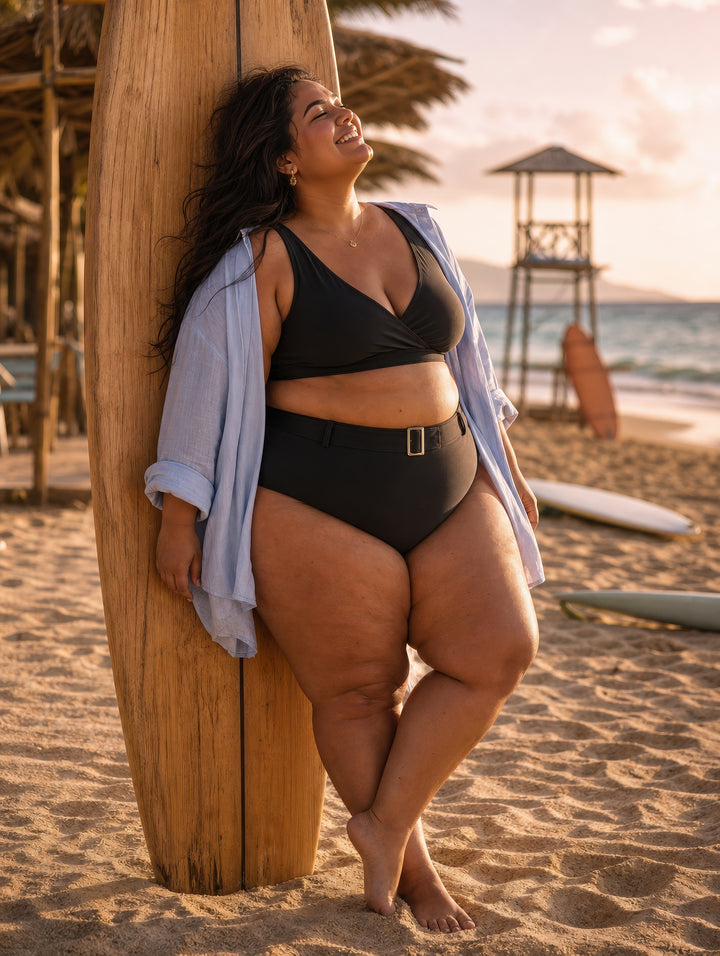 Woman in black swimsuit standing on a beach with sunset and surfboards in the background